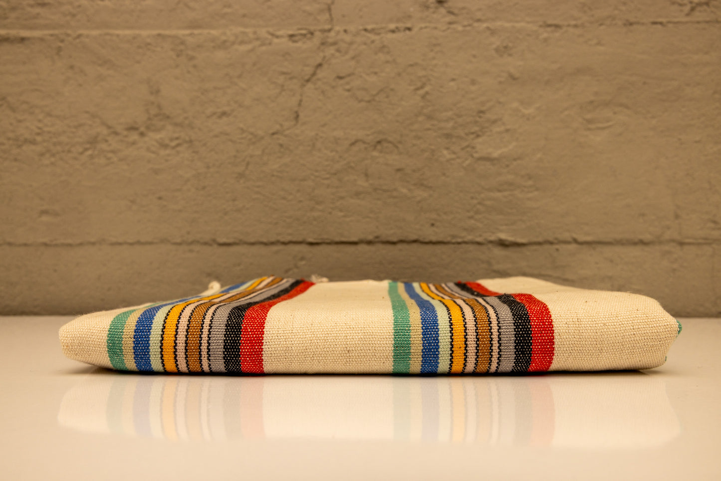 handwoven colorful striped towel on a reflective surface and beige background