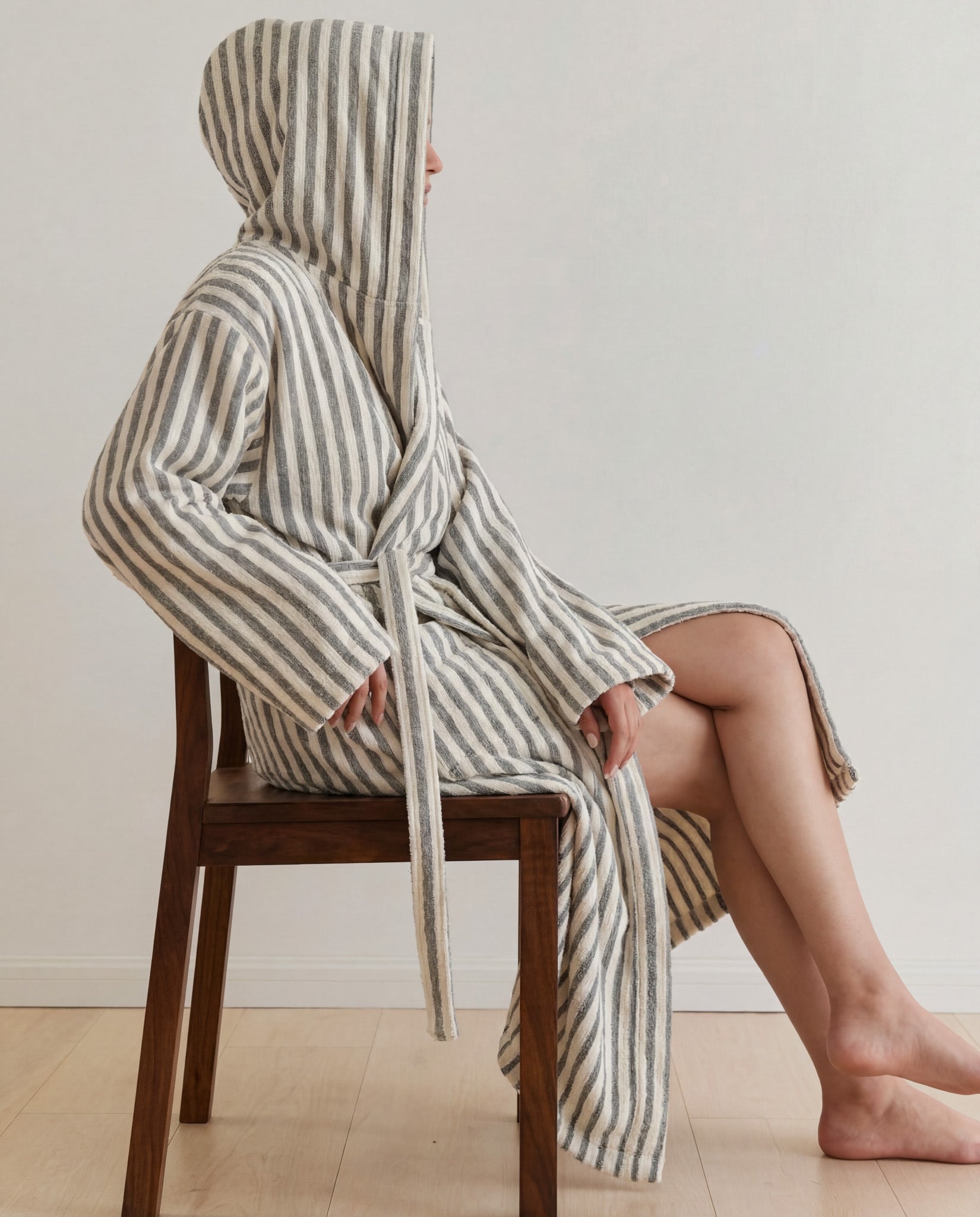 Person sitting on a chair wearing a gray striped robe with a hood.