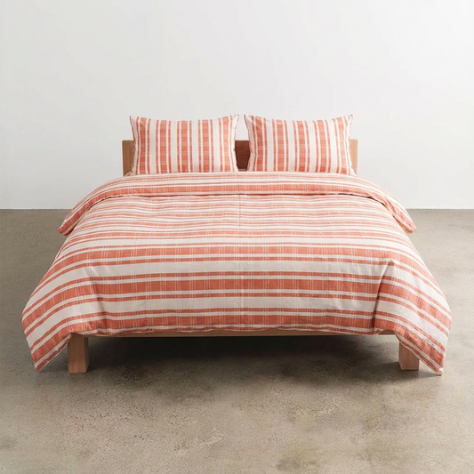 Bed with terracotta and white striped atelier orea bedding on a plain background