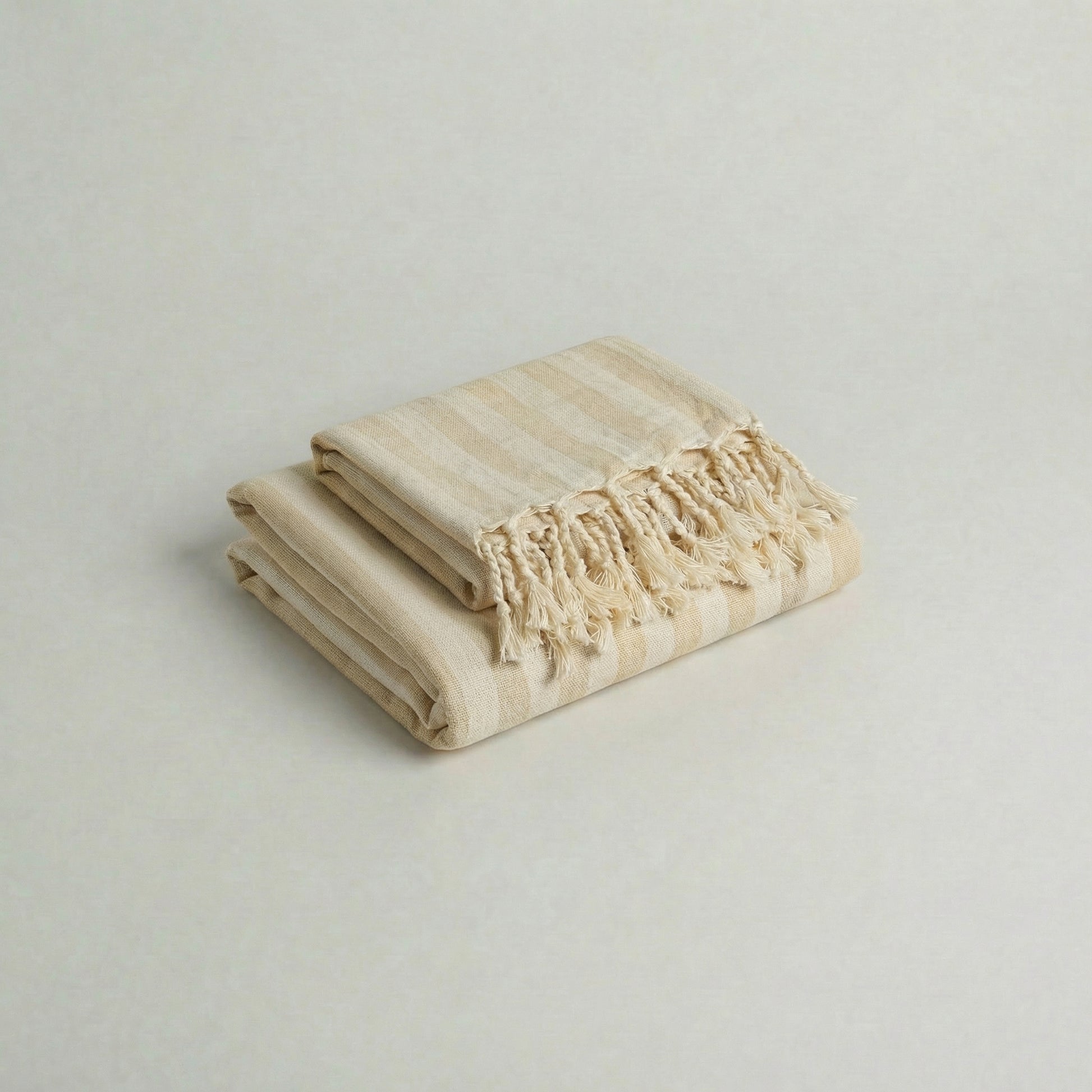 Handwoven atelier orea cotton towel set in ecru with beige stripes and tassels on a ligt background