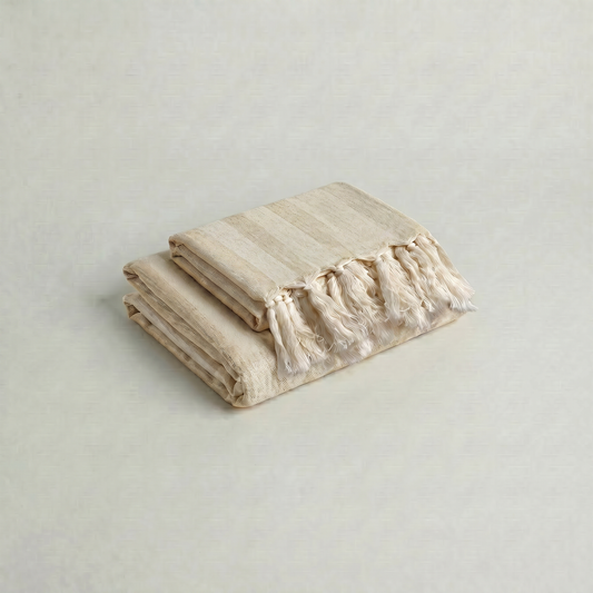 Folded beige handwoven cotton towel set with ruffled edge on a light gray background