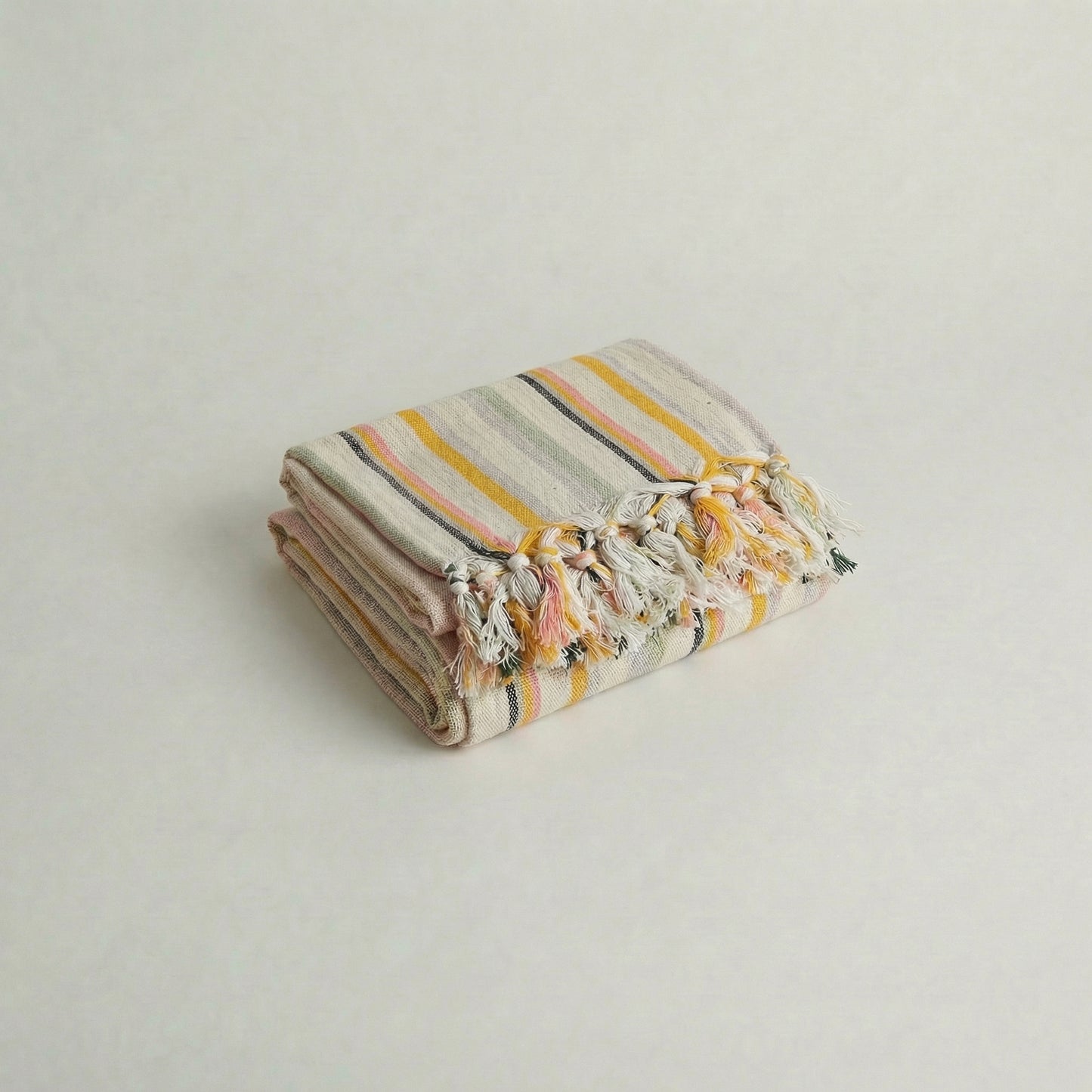 Folded handwoven cotton towel with pastel pink, blue, yellow, green stripes with tassels on a light background