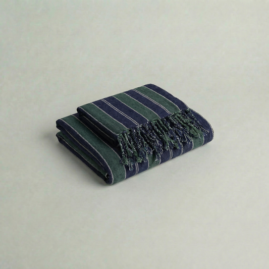 Folded handwoven atelier orea cotton towel in dark green and navy with fringes on a light gray background