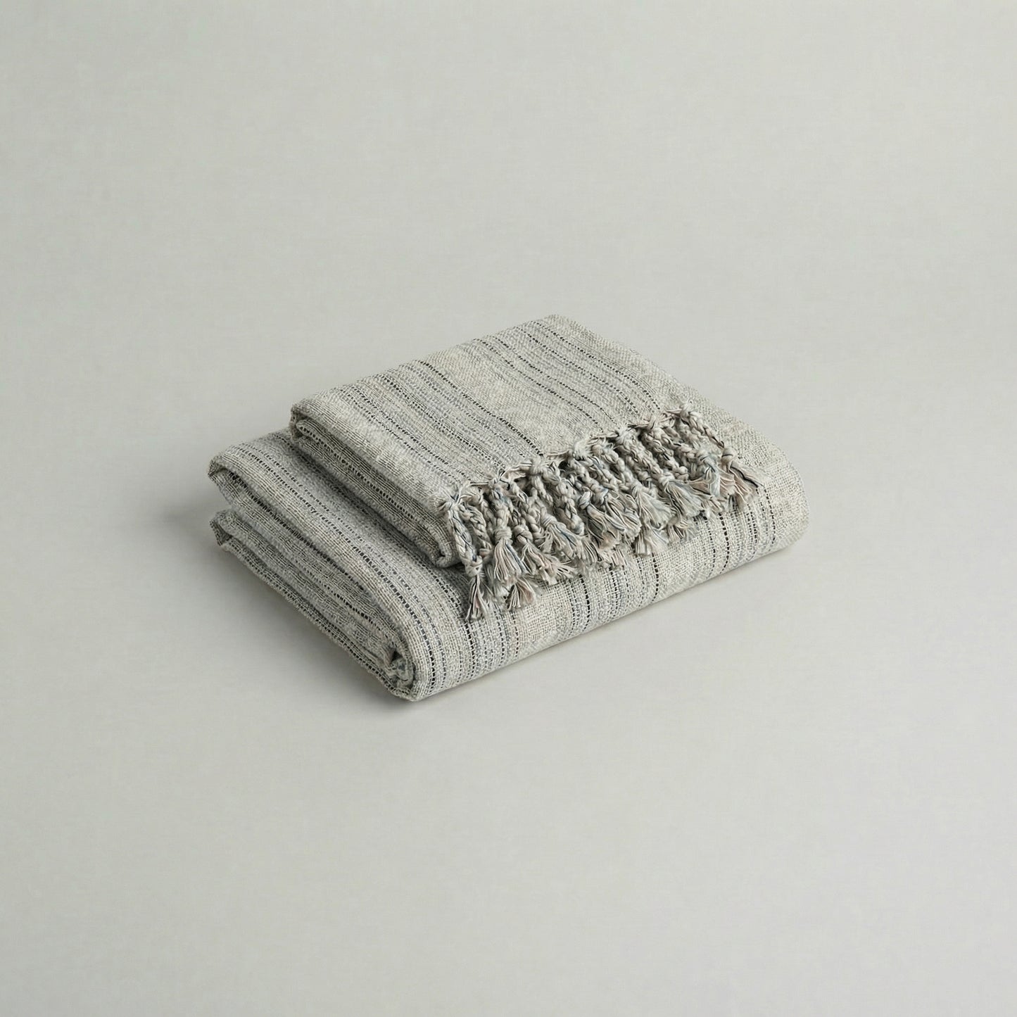 Folded slub cotton handwoven towel set with tassels on a light gray background