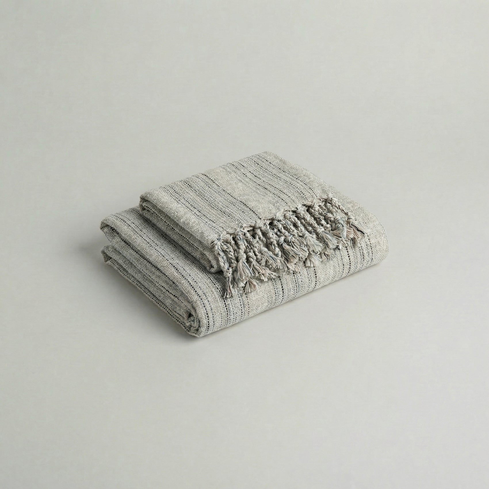 Folded slub cotton handwoven towel set with tassels on a light gray background