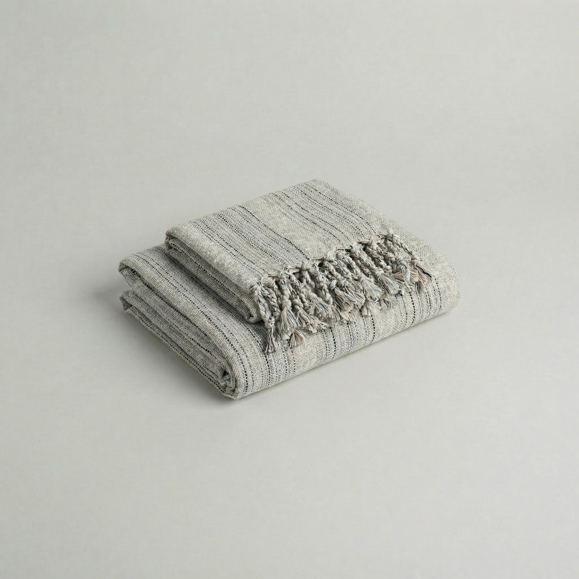 Folded slub cotton handwoven towel set with tassels on a light gray background