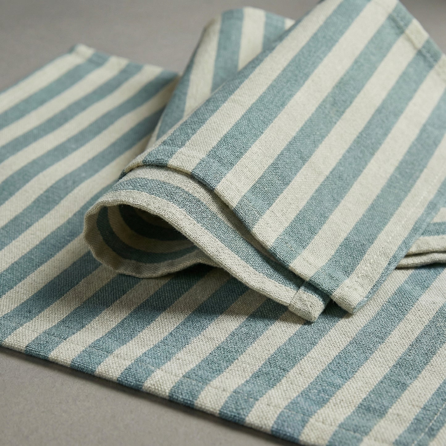 Rolled-up baby blue and white striped napkin and placemat on a gray surface