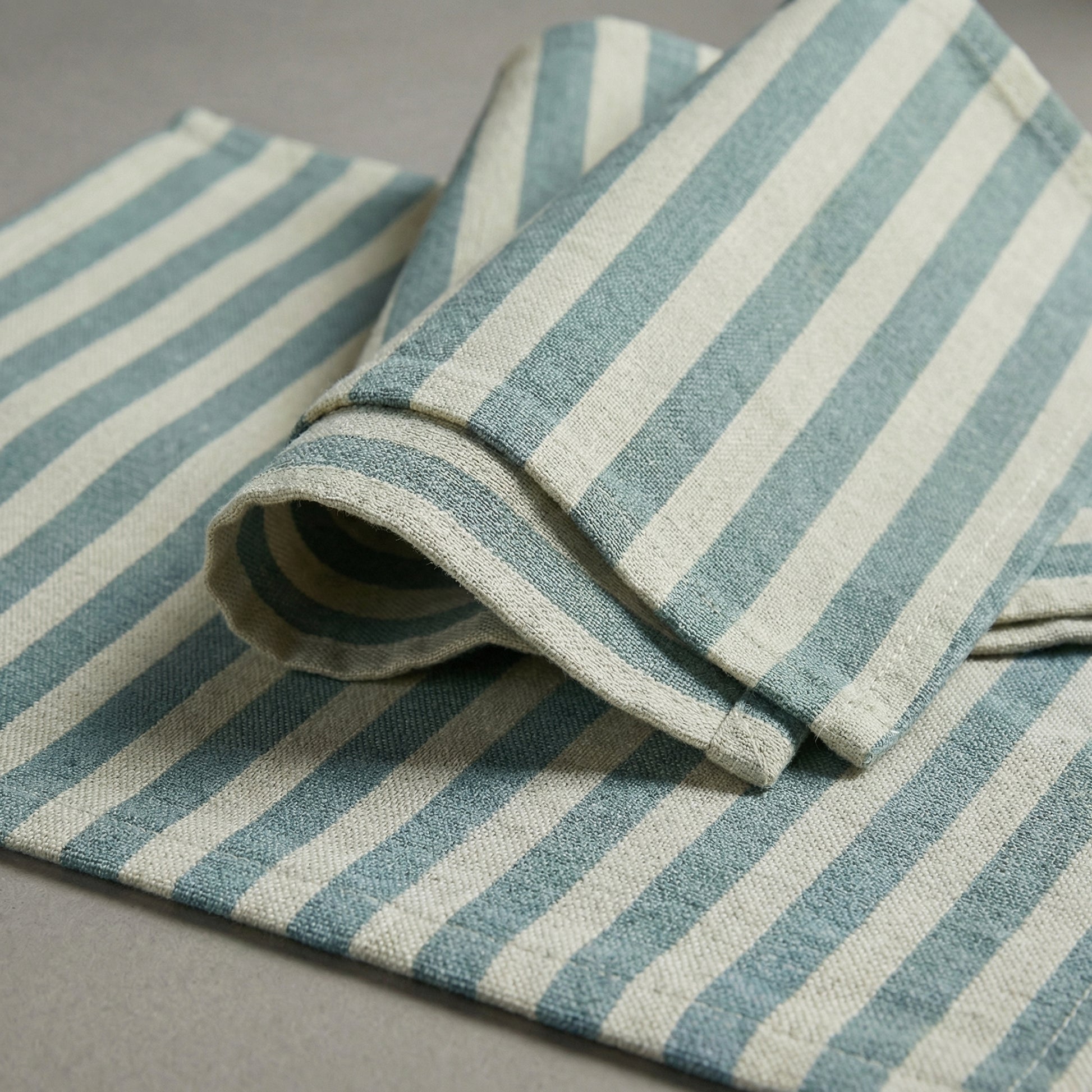 Rolled-up baby blue and white striped napkin and placemat on a gray surface