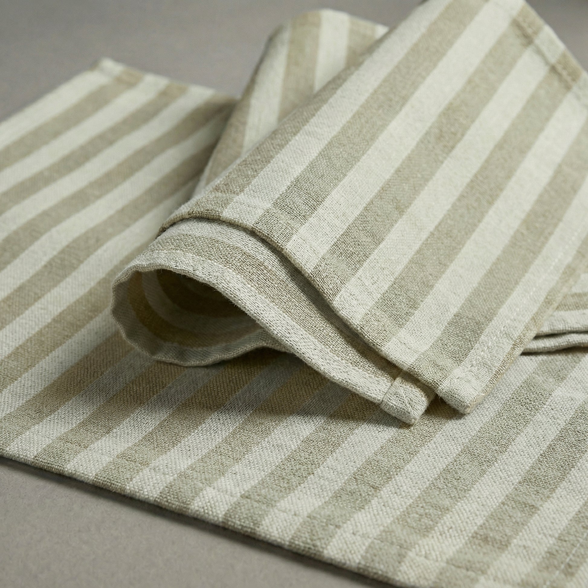 Folded ecru and beige striped cotton placemat and napkin on a gray surface