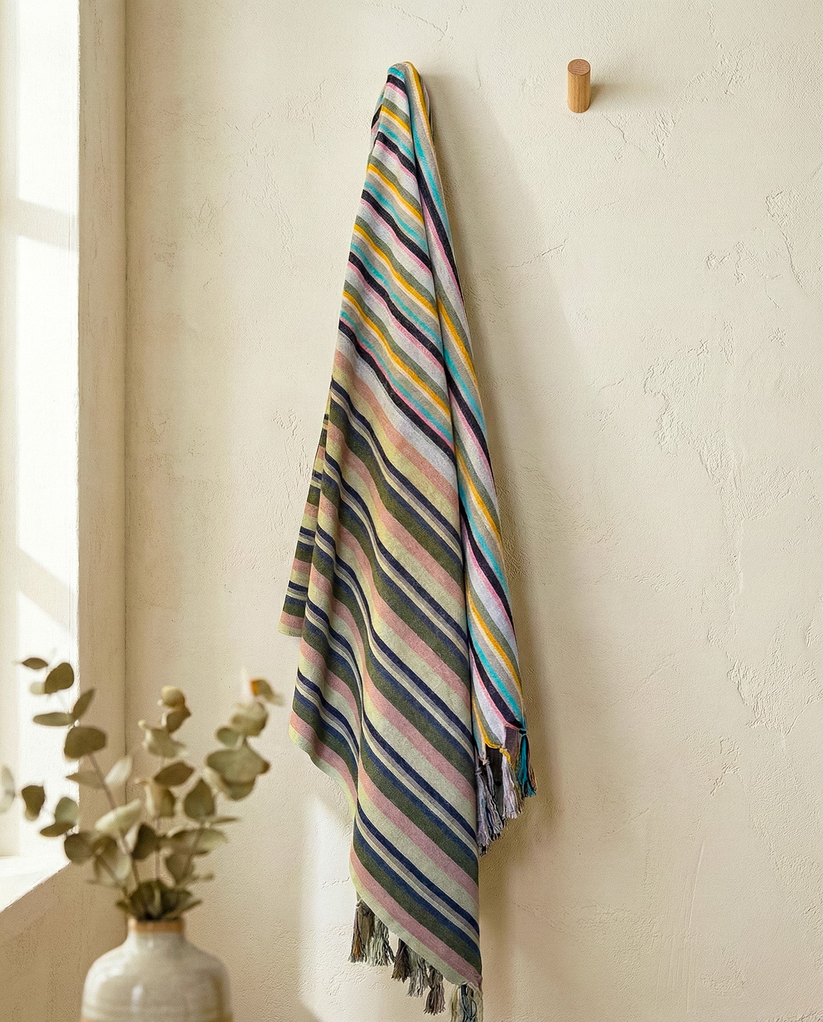 Striped towel hanging on a hook against a white wall with a vase of plants.