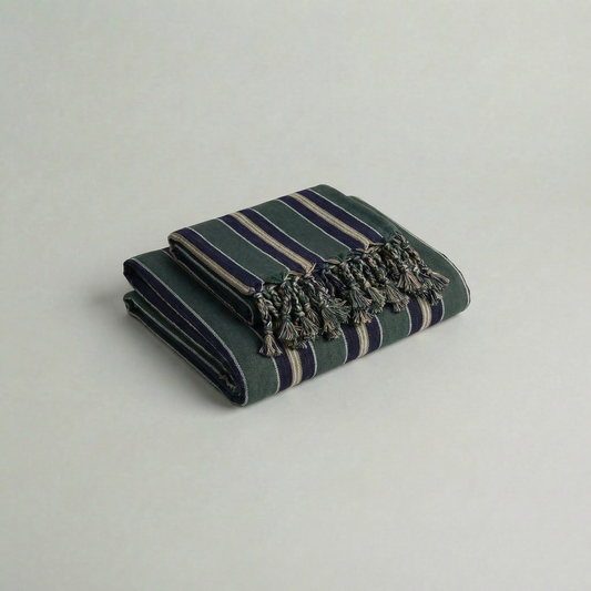 Folded handwoven atelier orea cotton towel in navy, dark green stripes with tassels on a light gray background