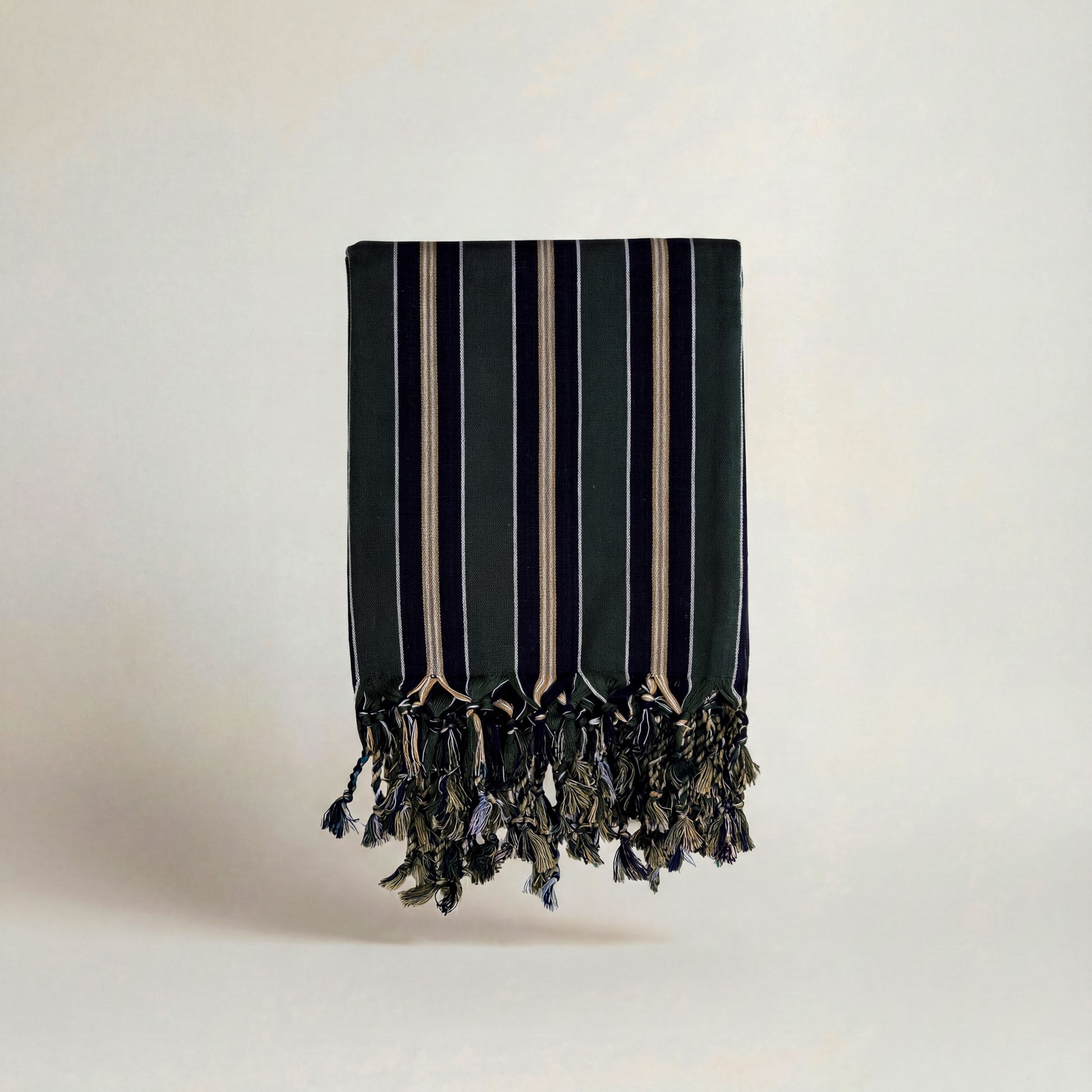 Striped navy dark green handwoven atelier orea towel with tassels on a light gray background