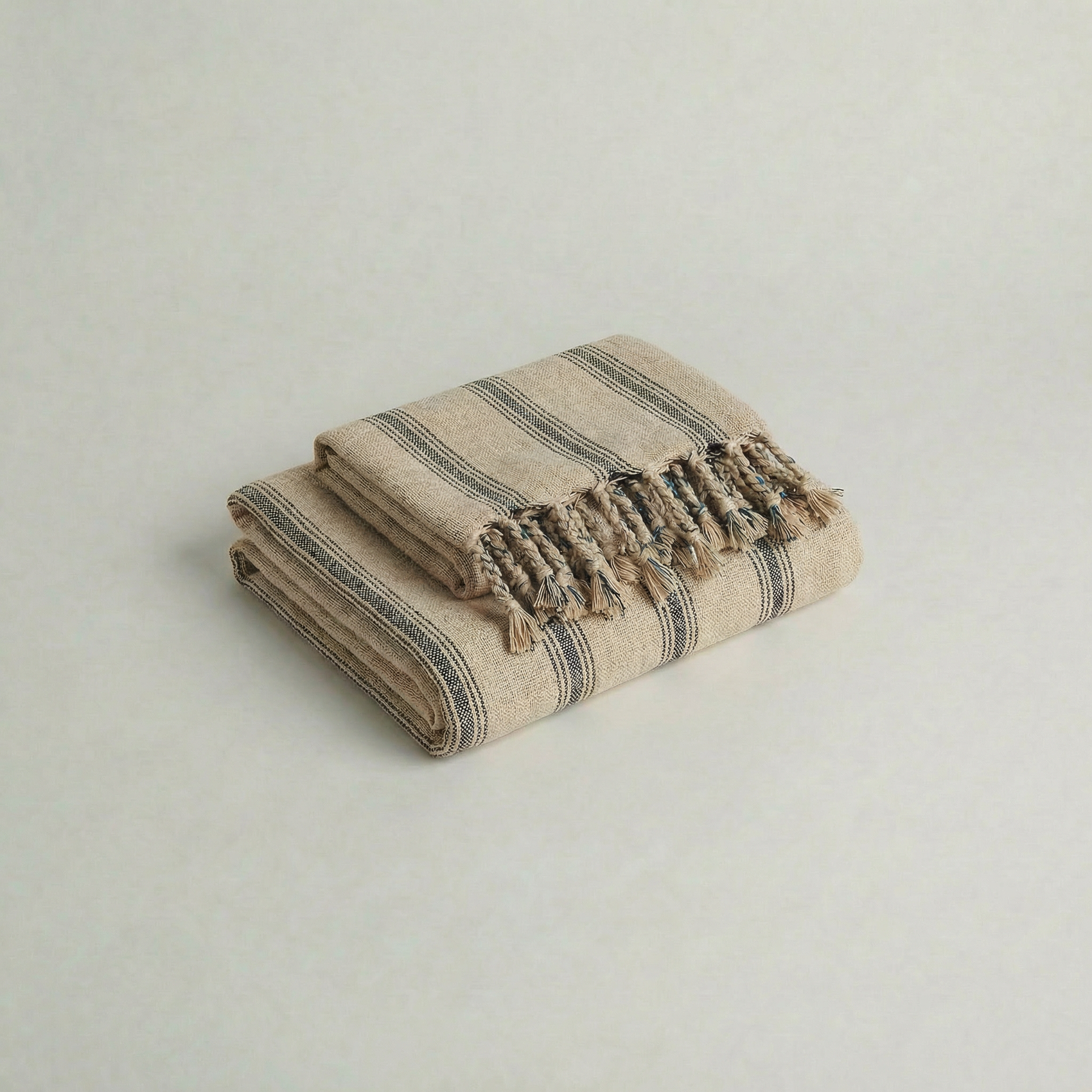 Folded handwoven slub cotton atelier orea beige and gray striped towel with tassels on a light gray background