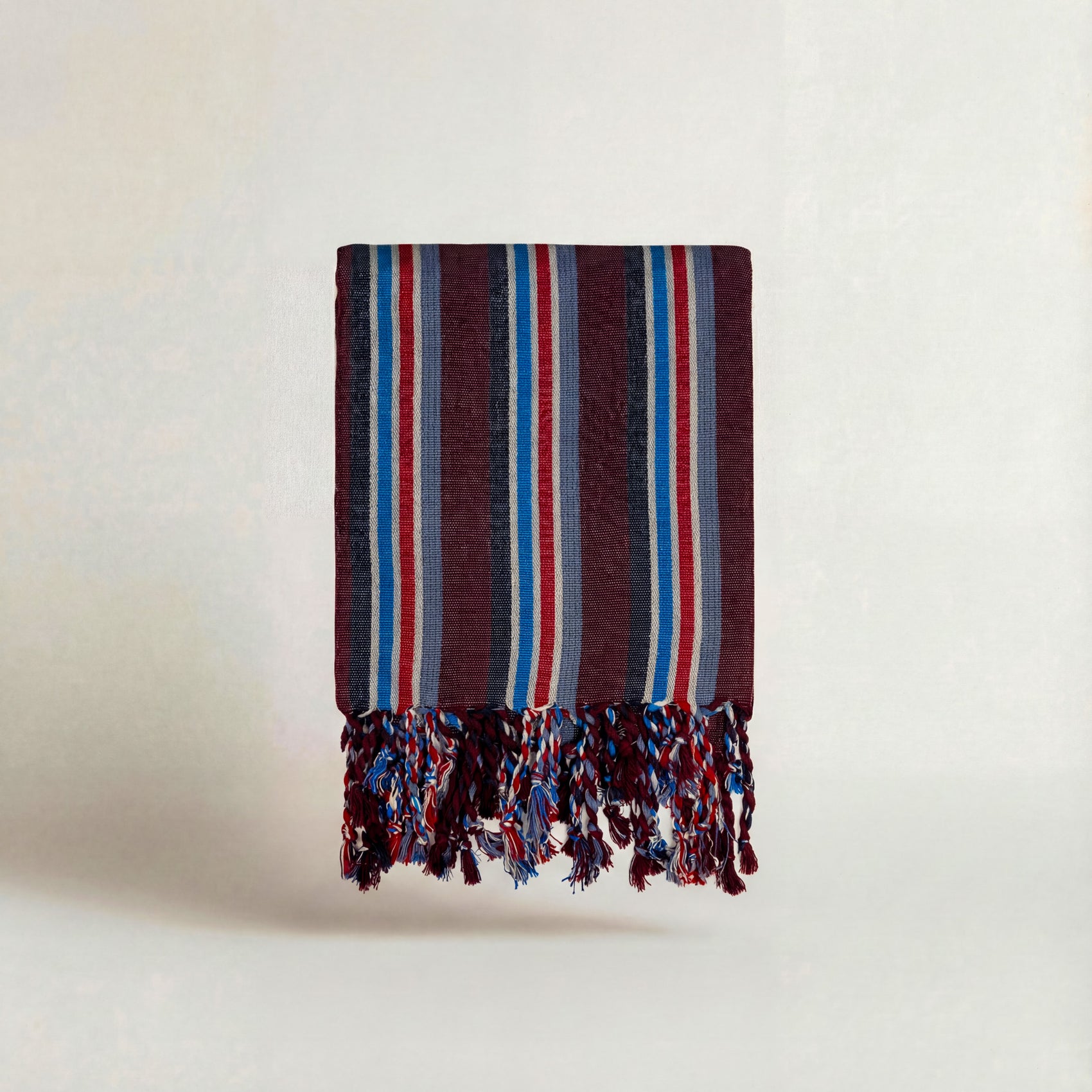 Striped maroon red blue white handwoven atelier orea towel with fringes on a light background
