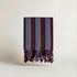 Striped maroon red blue white handwoven atelier orea towel with fringes on a light background