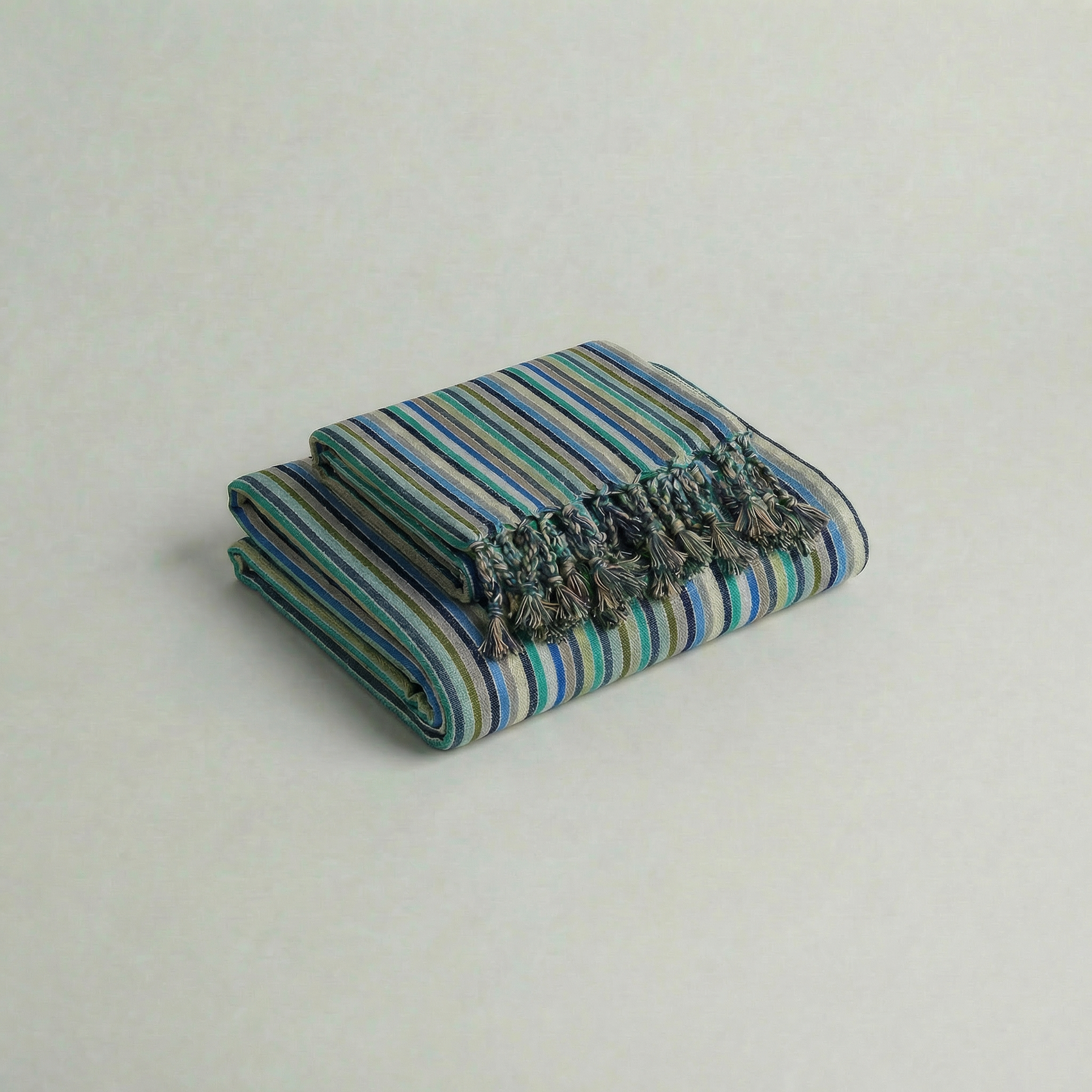 Striped handwoven cotton atelier orea towel in blue, turquoise, cyan striped with tassels on a light gray background
