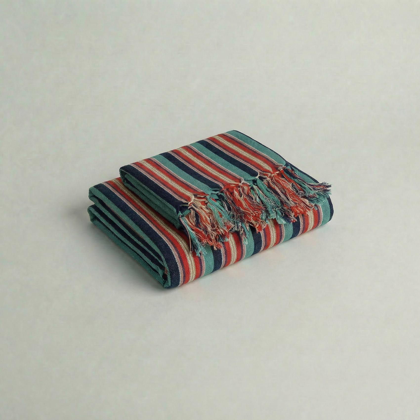 Folded striped handwoven cotton atelier orea towel with fringes on a light gray background