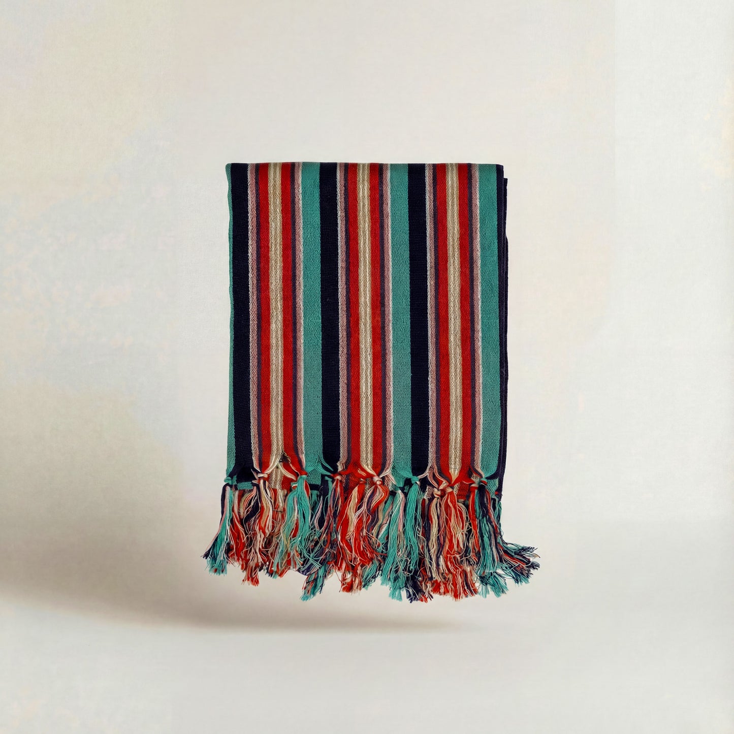 Striped handwoven atelier orea towel in red turquoise navy with tassels on a light background