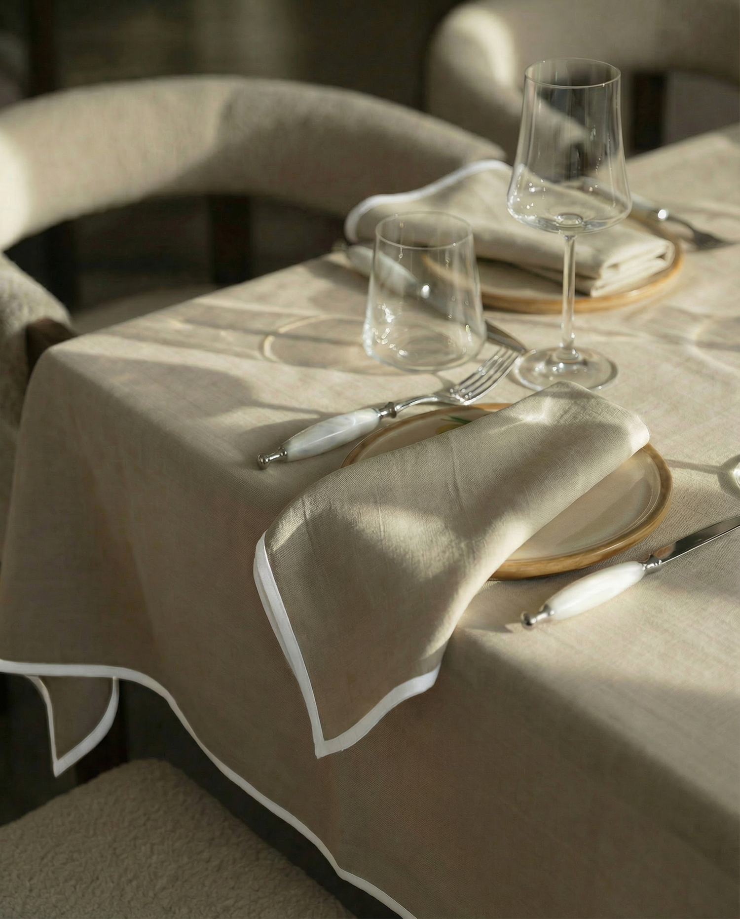 Dining table setting with beige turkish cotton tablecloth, plates, glasses, and cutlery.