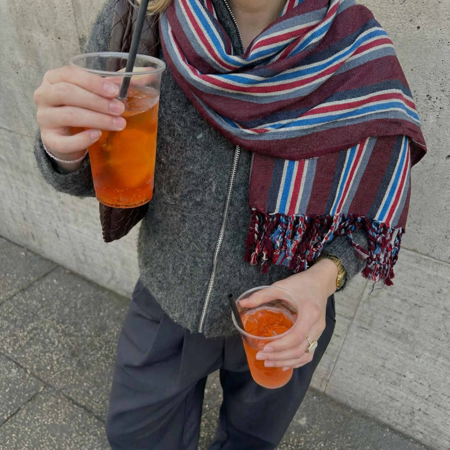 Person holding two drinks with straws, wearing a striped atelier orea cotton towel and gray coat