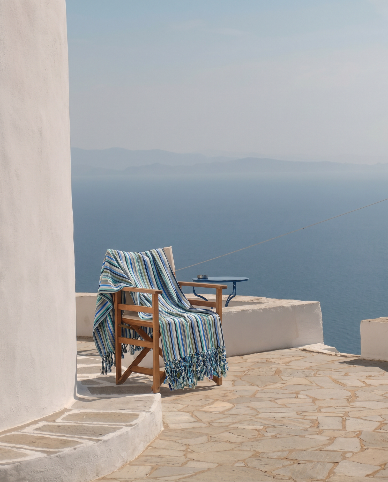 Chair with a handwoven blue striped cotton towel on a stone patio overlooking the ocean.