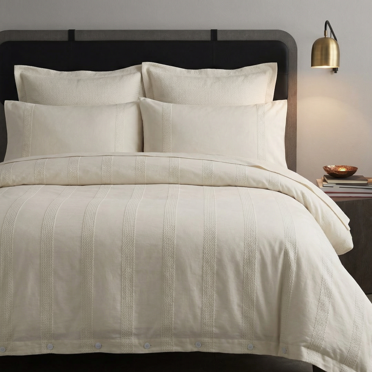 Beige textured bedding set on a bed with pillows and a lamp in the background.