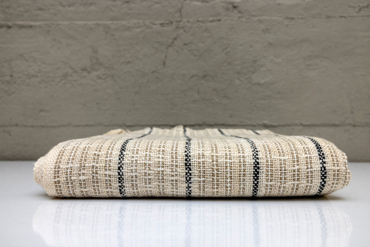 Folded handwoven turkish cotton towel with black stripes on a white surface and gray background
