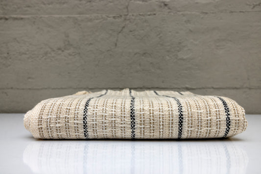 Folded handwoven turkish cotton towel with black stripes on a white surface and gray background