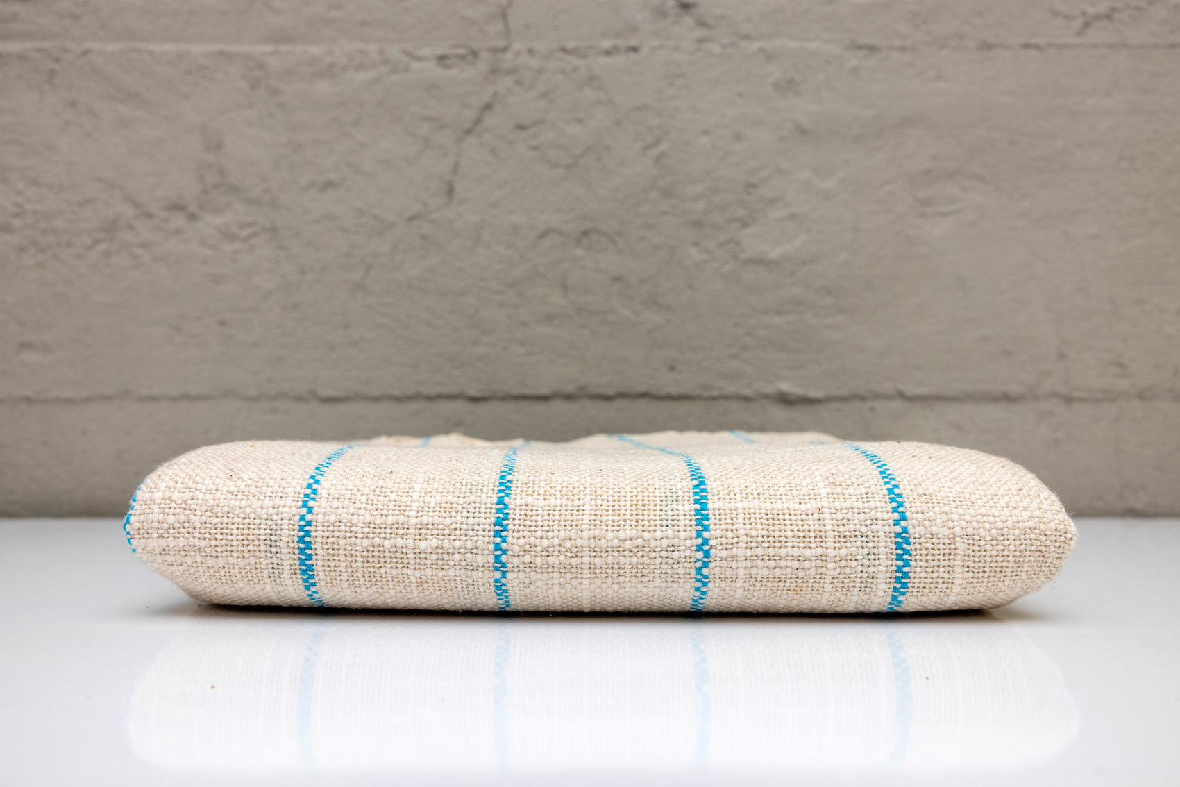 Folded atelier orea handwoven turkish cotton towel with blue stripes on a white surface and gray background