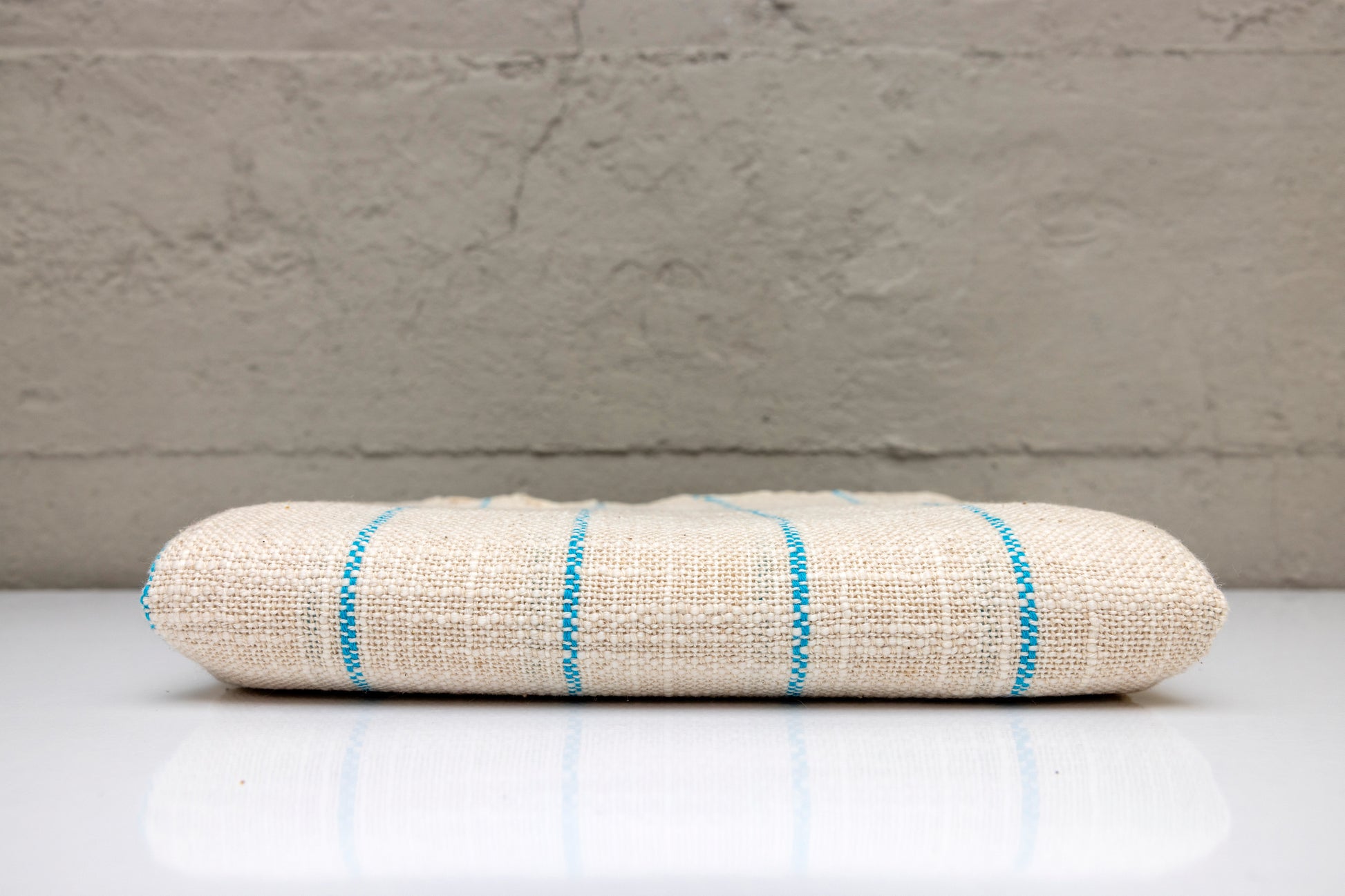 Folded atelier orea handwoven turkish cotton towel with blue stripes on a white surface and gray background