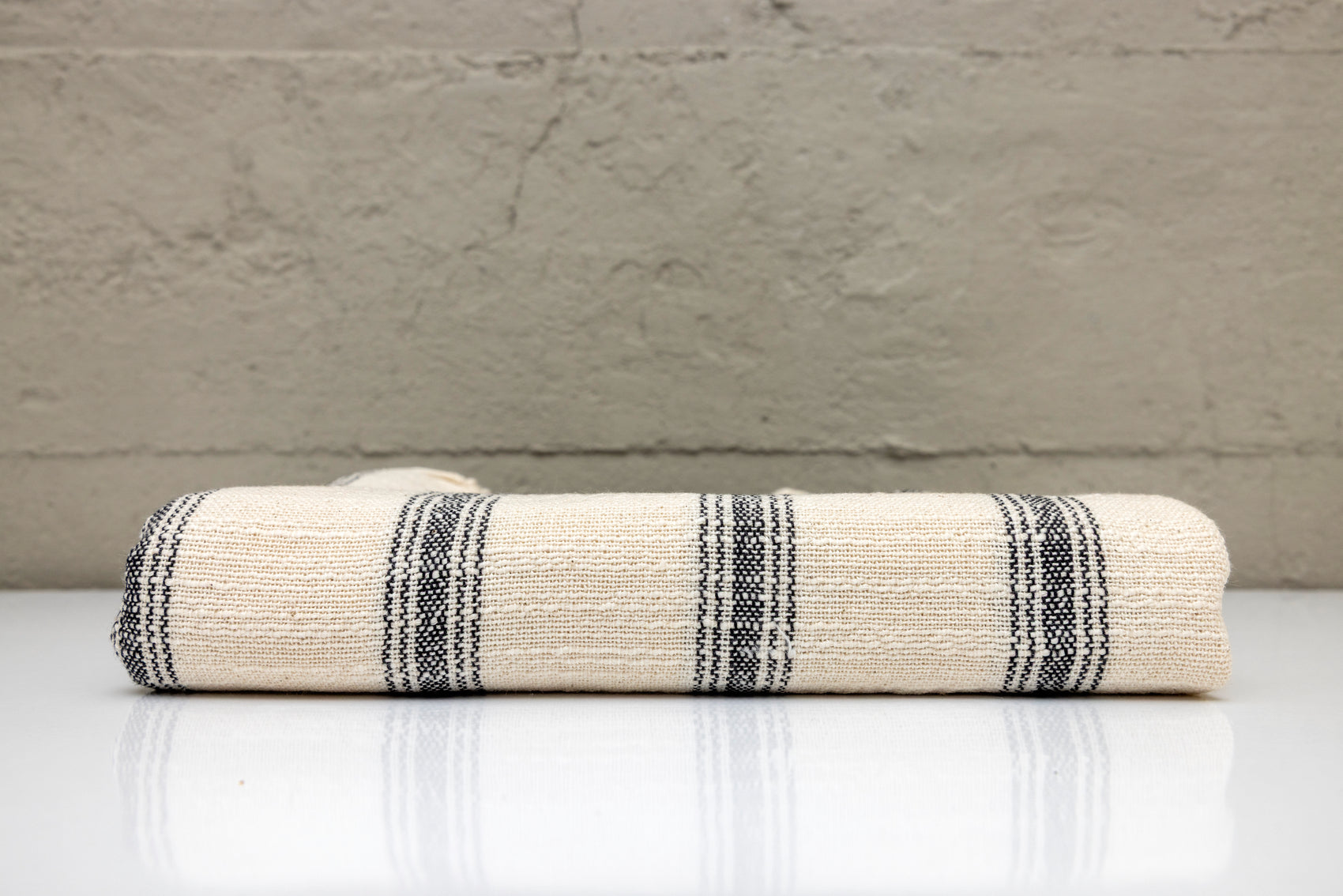 Folded atelier orea handwoven turkish cotton towel with black stripes on a white surface against a gray wall