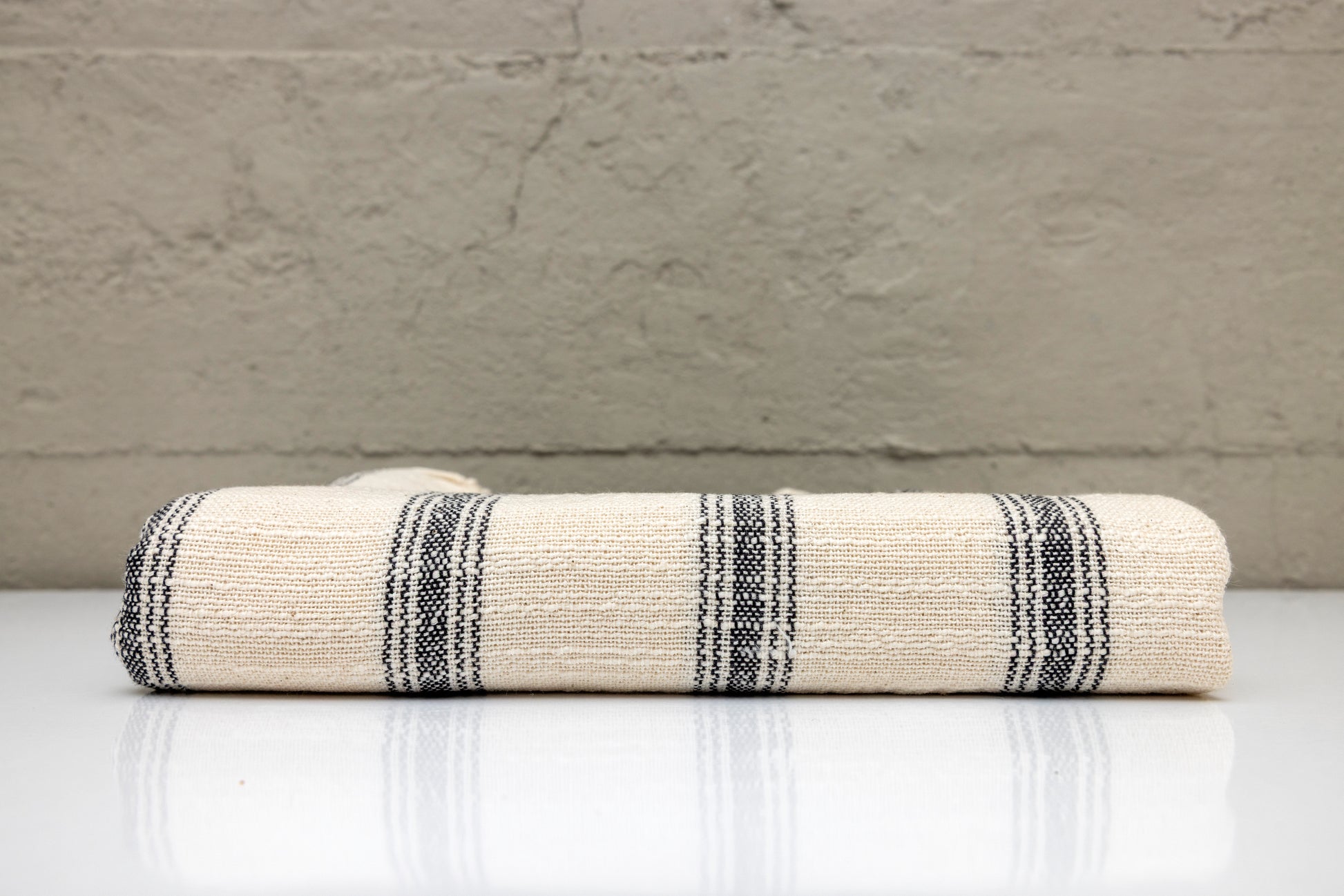 Folded atelier orea handwoven turkish cotton towel with black stripes on a white surface against a gray wall