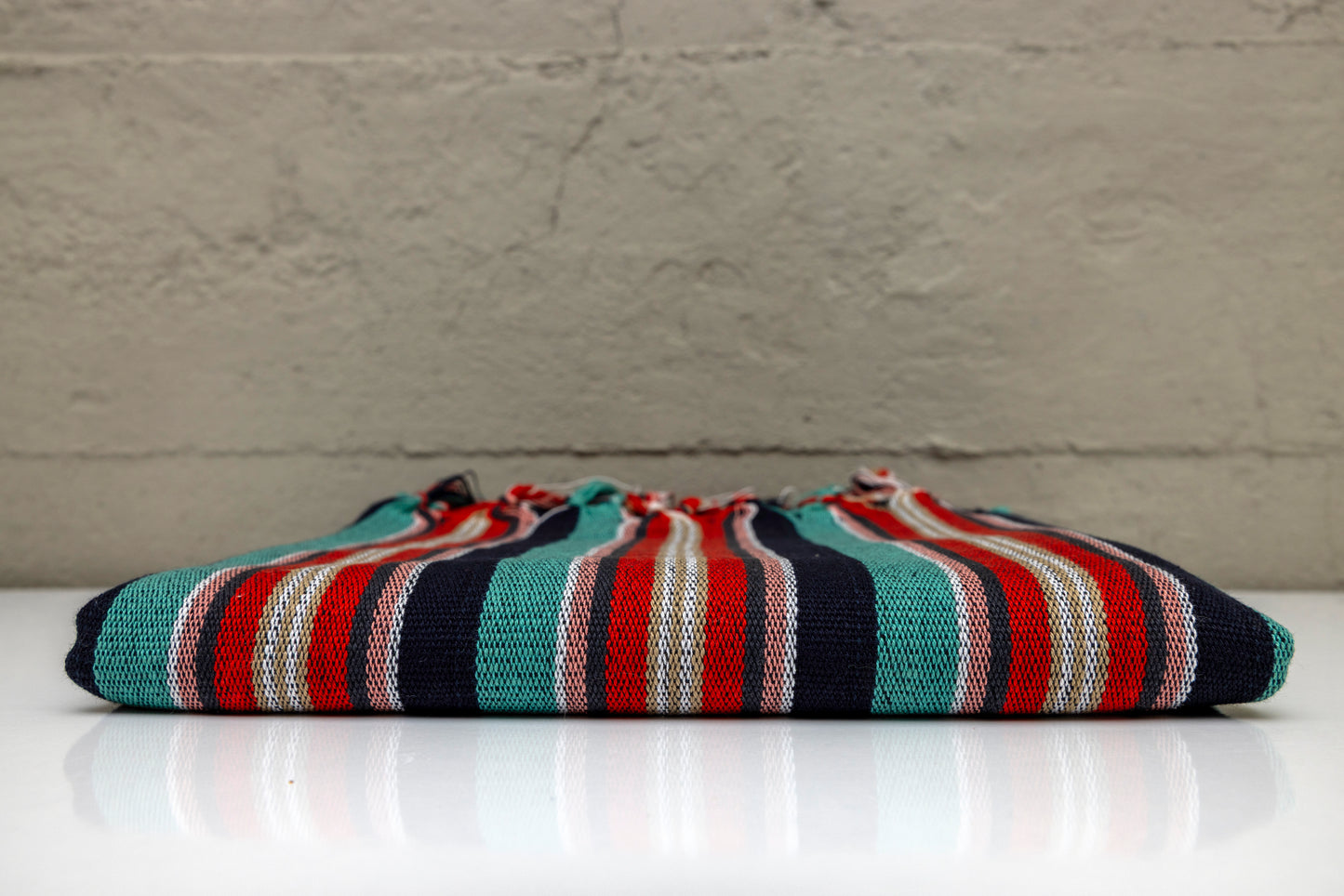 Folded atelier orea handwoven turkish cotton towel with red, turquoise, navy and black pattern on a white surface with gray background