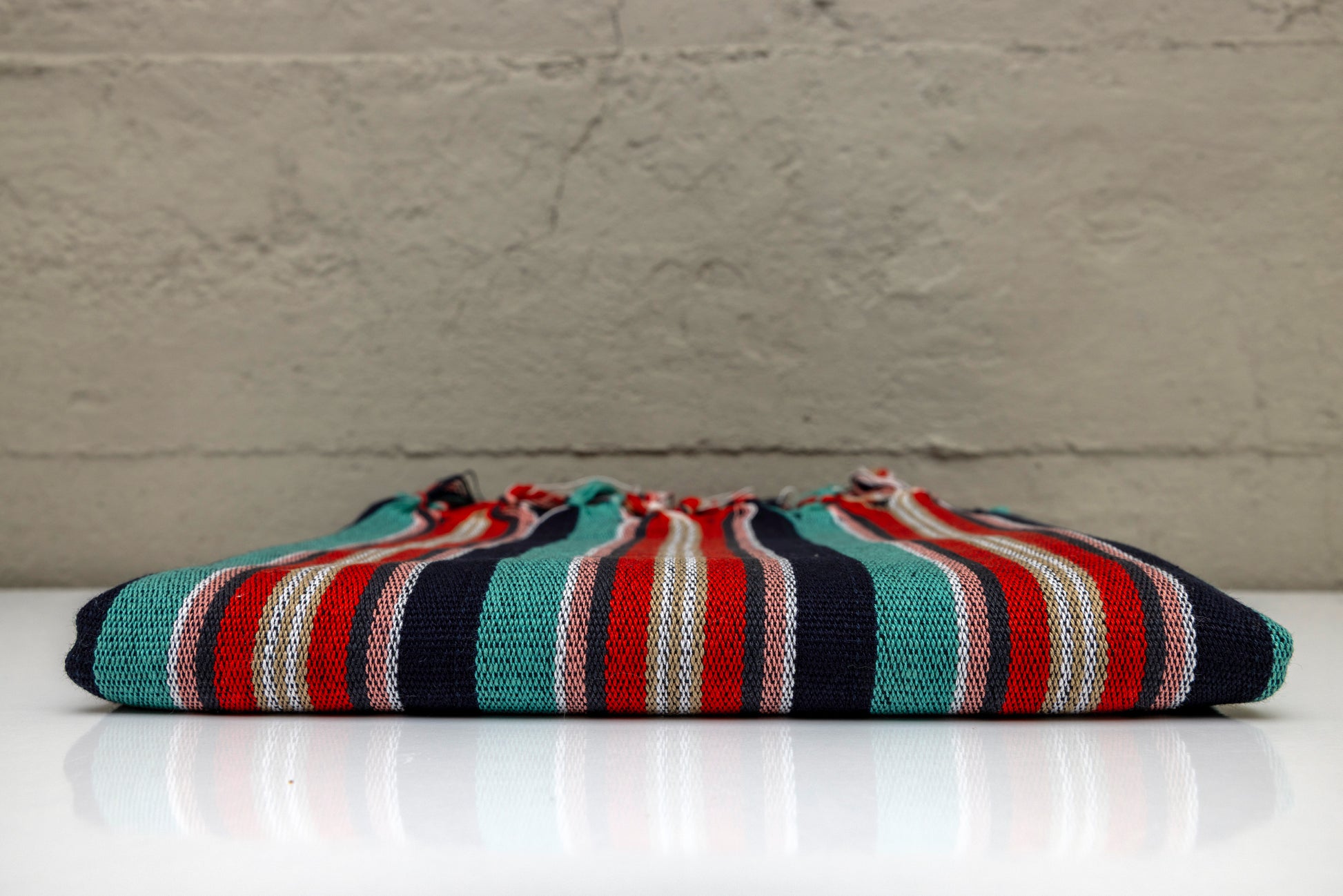 Folded atelier orea handwoven turkish cotton towel with red, turquoise, navy and black pattern on a white surface with gray background