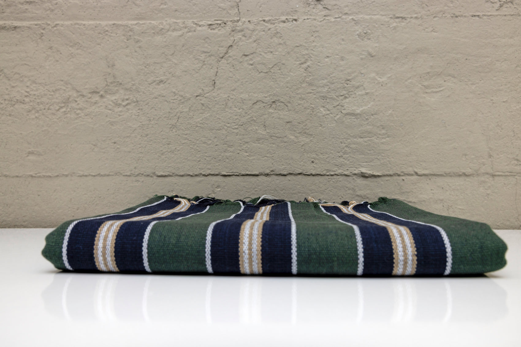 Folded atelier orea handwoven turkish cotton towel with dark green navy and beige stripes with a white surface with a gray textured wall background