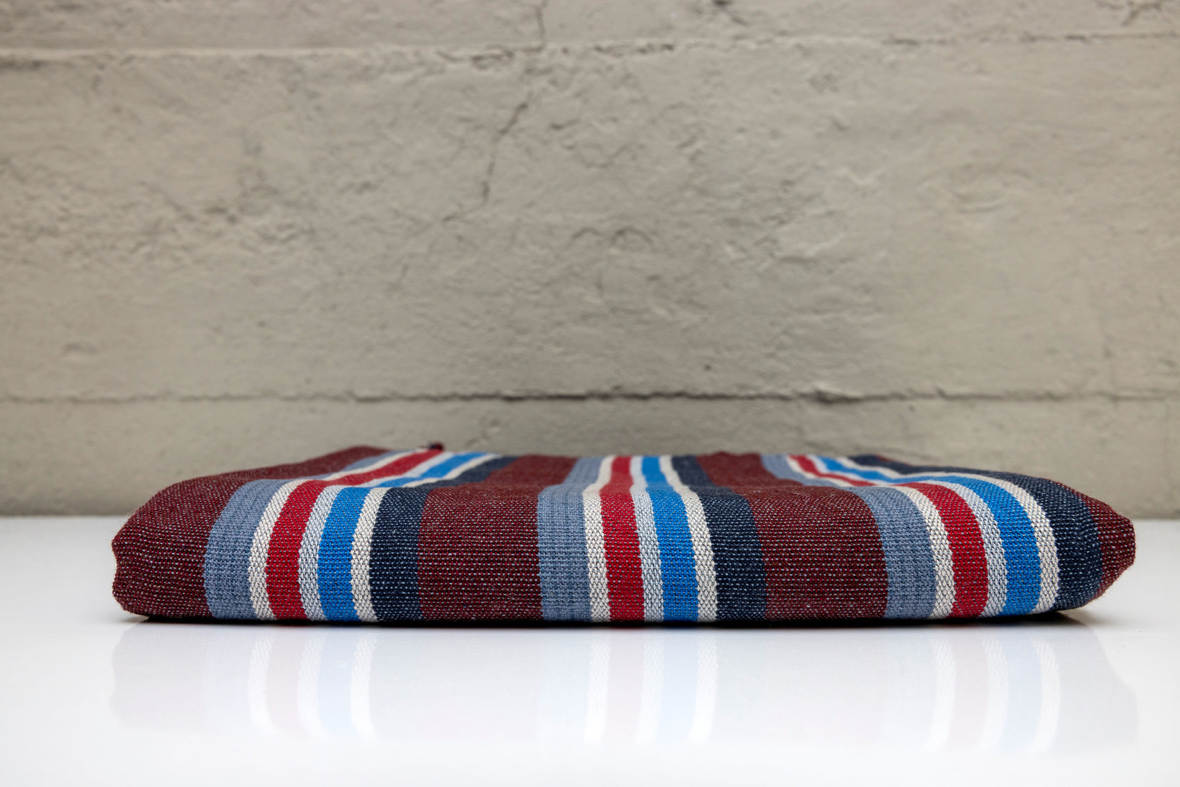 Folded atelier orea handwoven turkish cotton towel with striped brown, blue, and red colors on a white surface and gray background.