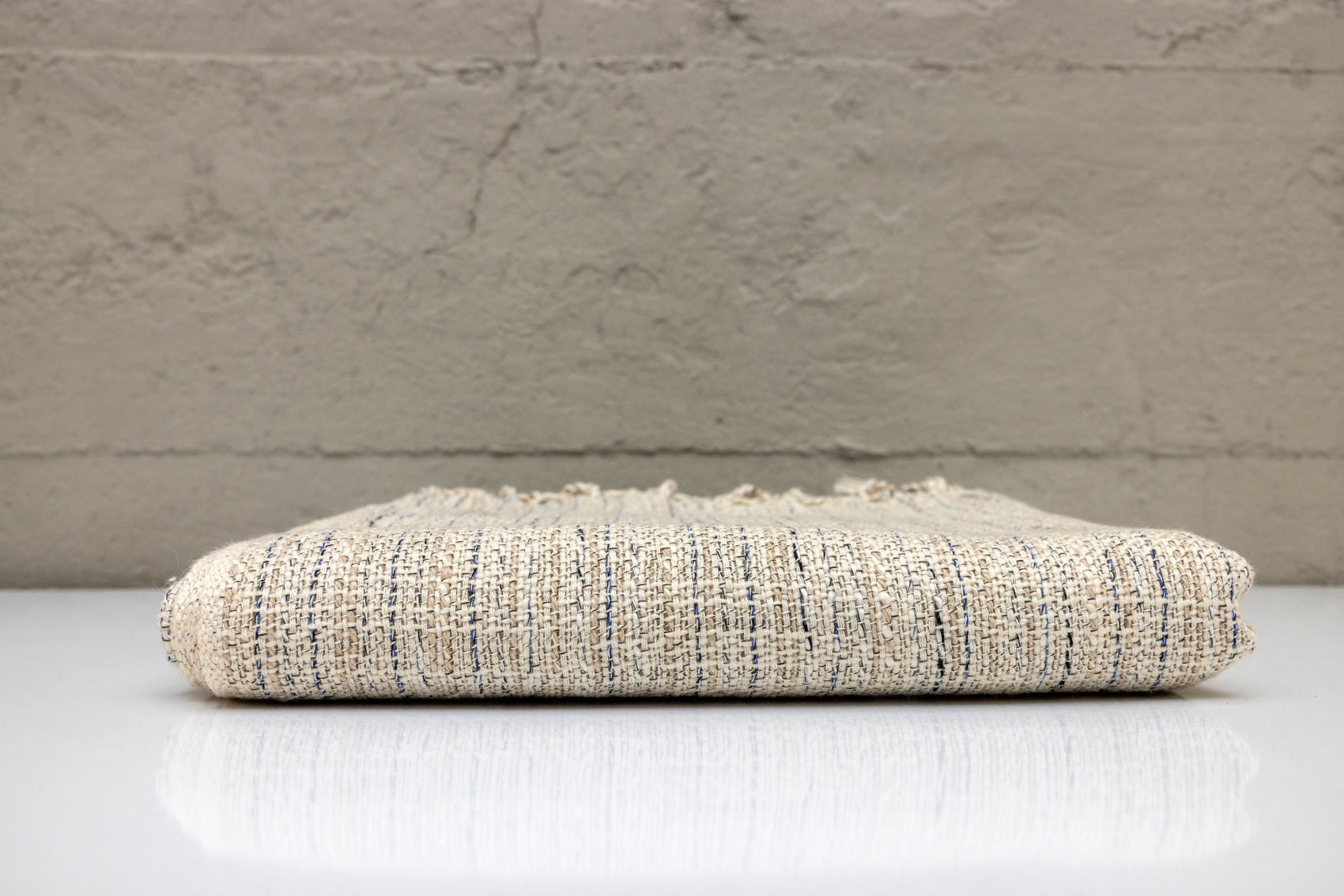 Folded atelier orea handwoven turkish cotton towel with natural colors on a white surface and gray background.