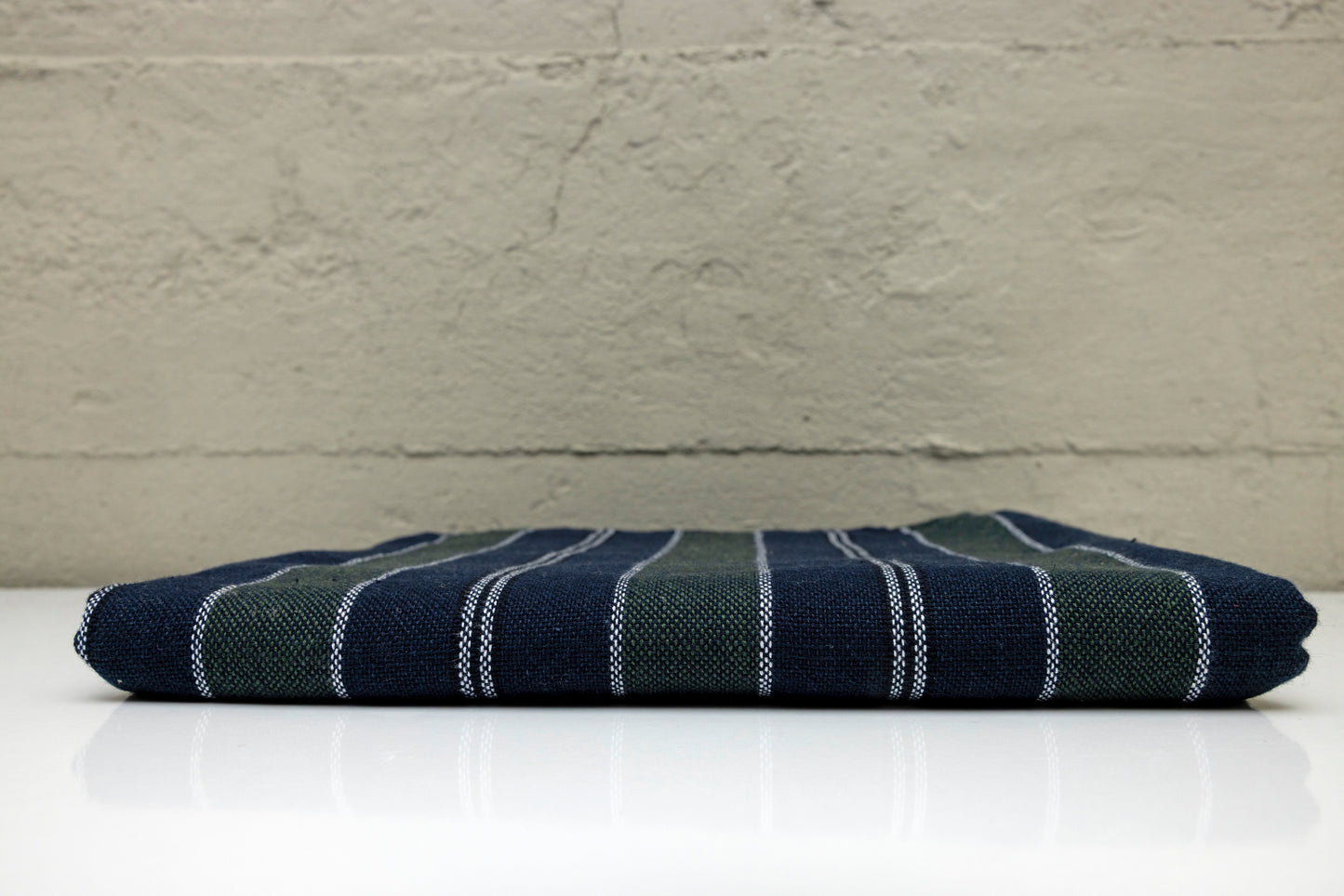 Folded atelier orea handwoven turkish cotton towel withnavy and dark green stripes on a white surface with a gray background