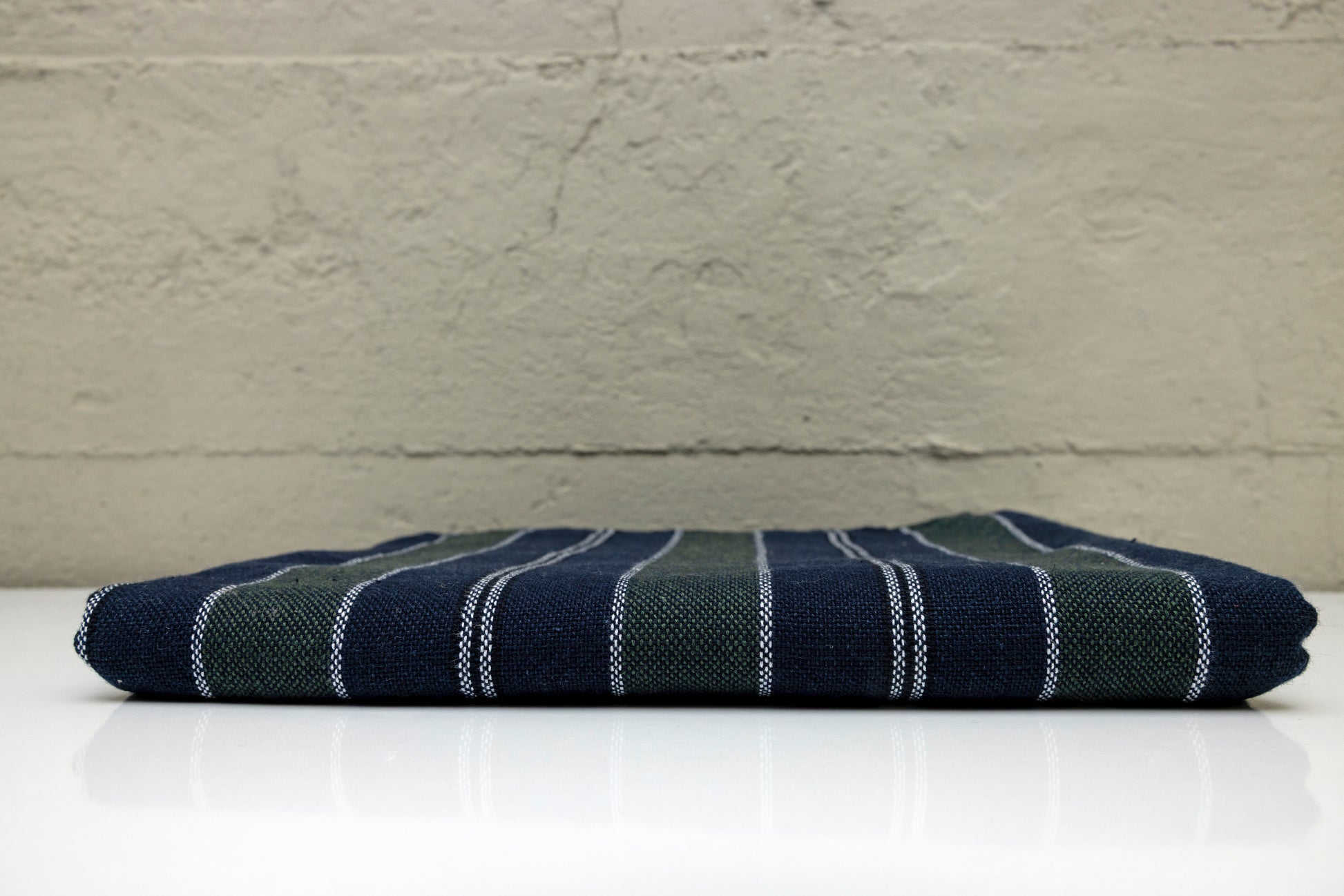 Folded atelier orea handwoven turkish cotton towel withnavy and dark green stripes on a white surface with a gray background