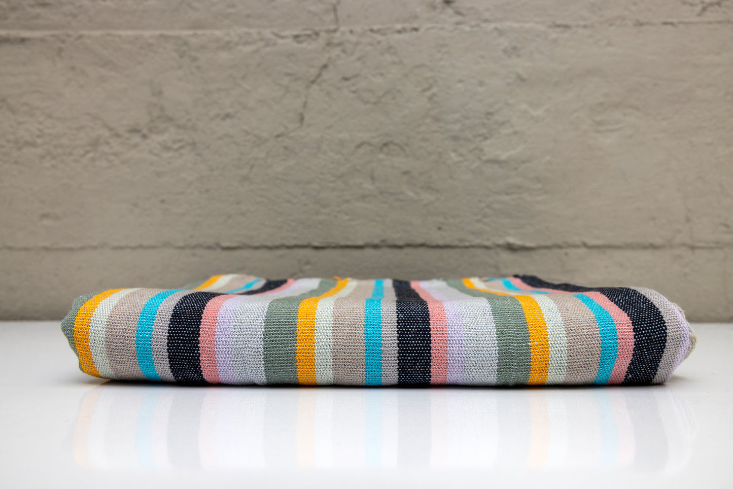 Folded atelier orea handwoven turkish cotton towel with mlti color stripes on a white surface with a gray background