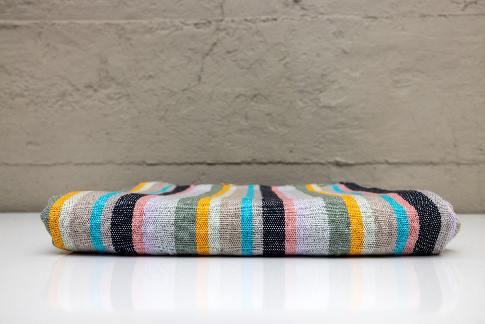 Folded atelier orea handwoven turkish cotton towel with mlti color stripes on a white surface with a gray background