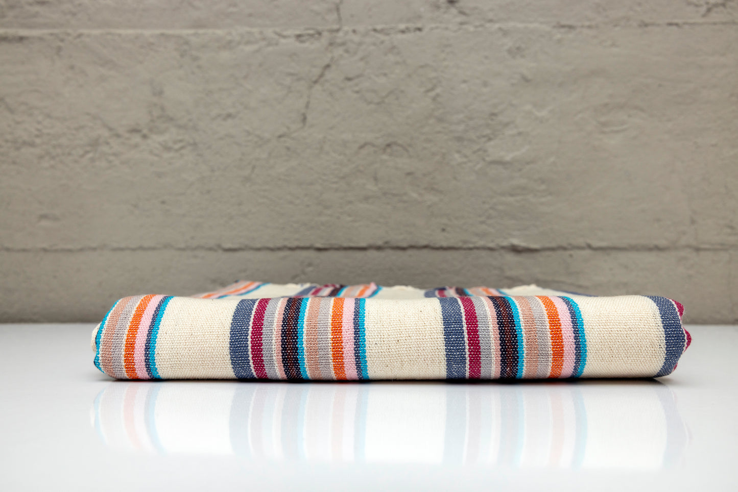 Folded atelier orea handwoven turkish cotton towel with multi color stripes on a white surface with a gray background