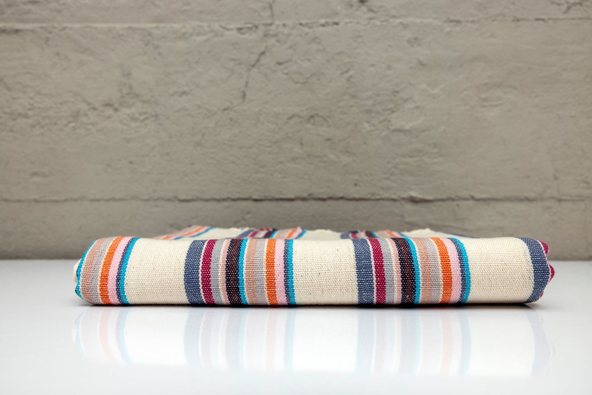 Folded atelier orea handwoven turkish cotton towel with multi color stripes on a white surface with a gray background