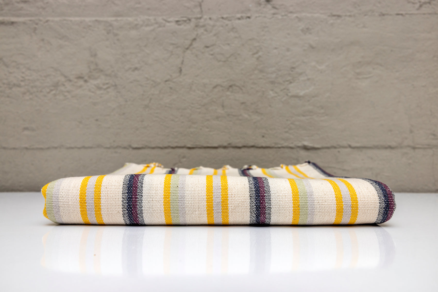 Folded atelier orea handwoven turkish cotton towel with yellow, purple, beige stripes on a white surface with a gray background