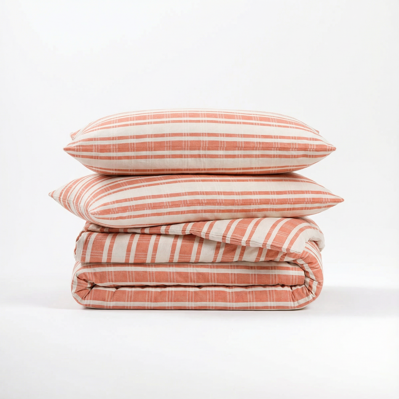 Stack of terracotta striped atelier orea bedding set with pillows on a white background