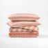 Stack of terracotta striped atelier orea bedding set with pillows on a white background